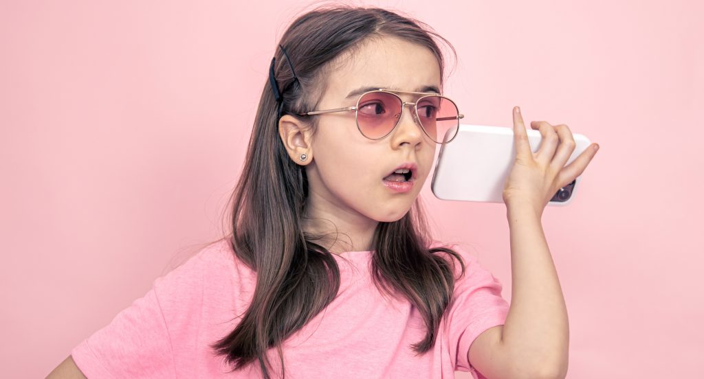 stylish little girl with smartphone on pink background